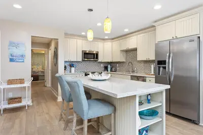 a kitchen with white cabinets and a stainless steel refrigerator at Beachfront Bliss - DMBC815 in Solana Beach