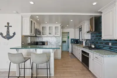 a kitchen with white cabinets and a island with bar stools at Beachfront Retreat with Ocean Views Private Rooftop Deck Walk to Pier and Town in Newport Beach