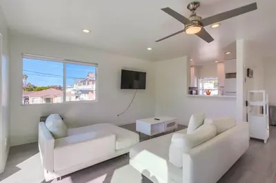 a living room with white furniture and a ceiling fan at 2nd floor A-C steps to beach downtown La Jolla in San Diego