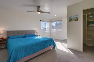 a bedroom with a bed with a blue comforter and two windows at 2nd floor A-C steps to beach downtown La Jolla in San Diego