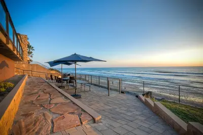 a patio with a table and an umbrella on the beach at Oceanfront Getaway - Ocean Views - Fire Pit - BBQ - Beach Access in Carlsbad