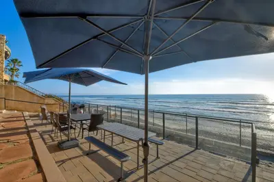 a patio with chairs and umbrellas on the beach at Oceanfront Getaway - Ocean Views - Fire Pit - BBQ - Beach Access in Carlsbad