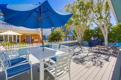 a table and chairs with a blue umbrella on a deck at Luxury summer house feet from bay & ocean patios in San Diego