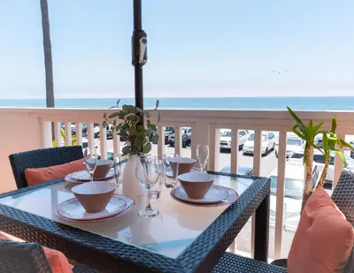 a table with plates and glasses on a balcony with the ocean at Beachwalk Villas in Carlsbad