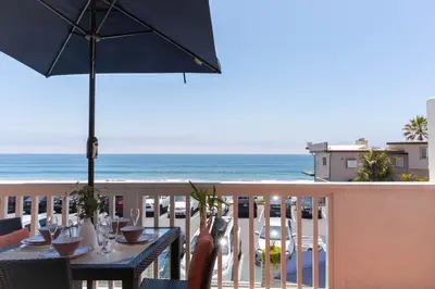 a table with an umbrella on a balcony with the ocean at Beachwalk Villas in Carlsbad