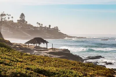 a beach with a straw umbrella and the ocean at Coastal Retreat 1BR Steps to Ocean & Peek Views in San Diego