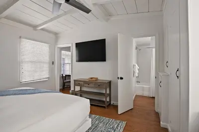 a white bedroom with a bed and a television on the wall at Beautiful Windansea Beach Compound Steps to Sand in San Diego