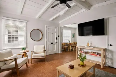 a living room with a flat screen tv and a table at Beautiful Windansea Beach Compound Steps to Sand in San Diego