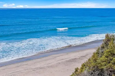 a surfer riding a wave on a beach at Sunglow Horizon - DMBC873B in Solana Beach