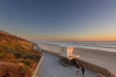 two people walking down a sidewalk next to the beach at 3636 Carlsbad Blvd - Lower in Carlsbad
