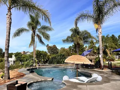 a pool with palm trees and chairs and an umbrella at Wine Country Villa in Temecula