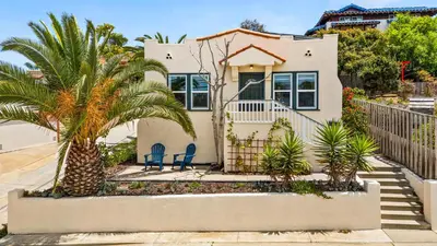 a house with two chairs and a palm tree at Cozy Ocean Beach Bungalow in San Diego