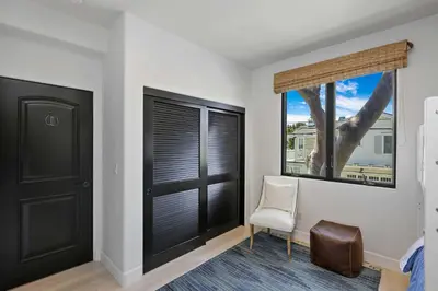 a bedroom with black doors and a white chair and a window at Poinsettia Palms - Chic & Luxe Patio Near Beach in Corona del Mar