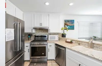 a kitchen with white cabinets and a stainless steel refrigerator at Seashore Sun and Fun - On Beach in Newport Beach