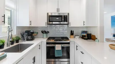 a white kitchen with a stove and a microwave at Coastal-Chic Newport Stay Steps to the Beach Dining Boardwalk Optional Add-On Unit in Newport Beach