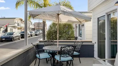 a table and chairs with an umbrella on a porch at Coastal-Chic Newport Stay Steps to the Beach Dining Boardwalk Optional Add-On Unit in Newport Beach