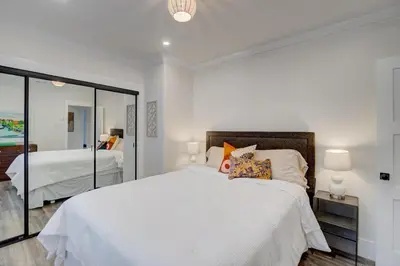 a white bedroom with a large bed and a mirror at Historic Barrio Logan Bungalow in San Diego