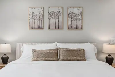 a bedroom with a white bed with three paintings on the wall at NEW Cozy Zen Pool Jacuzzi Home Heart of San Diego in San Diego