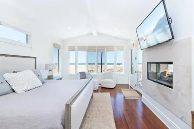 a white bedroom with a large bed and a fireplace at Oceanfront Escape with Breathtaking Views in Newport Beach