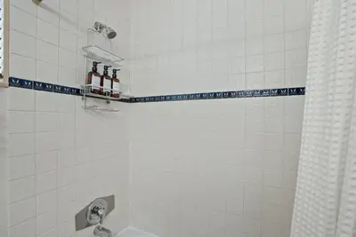 a white bathroom with a shower with bottles on a shelf at Dream 2 Story Home! Steps to the Ocean, Private Patio, AC, Hot Tub & BBQ in San Diego