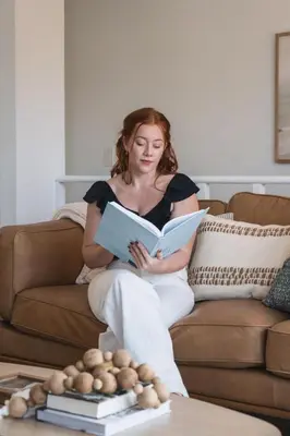a woman sitting on a couch reading a book at Boho Beach Bungalow Walk to the Beach in San Diego