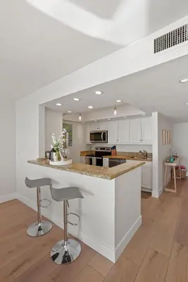 a kitchen with white cabinets and a counter with stools at Oceanfront Paradise with Sunset Balcony, Pool, Spa, Beach Access and Parking in San Diego