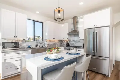 a kitchen with white cabinets and a kitchen island with chairs at Ocean View Roof Deck - Walk to the Beach & Pier in Oceanside
