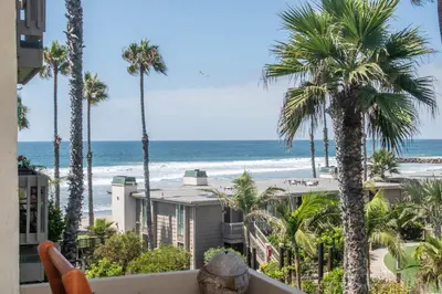 a view of the beach from a balcony with palm trees at Walk to the Beach Sunset Ocean Views - D-207 in Oceanside