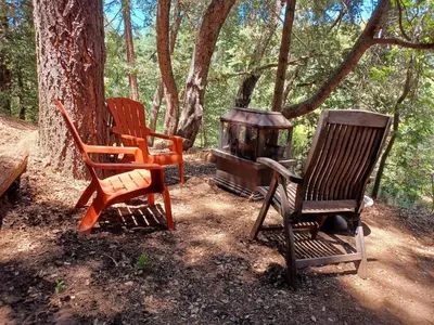 three chairs and a wood stove in the woods at Historic Holiday Redwood Cabin in Palomar Mountain, California in Palomar Mountain