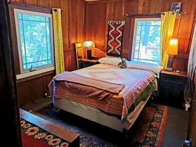 a bedroom with a bed and two windows at Historic Holiday Redwood Cabin in Palomar Mountain, California in Palomar Mountain