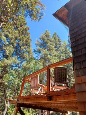 two chairs on a deck with trees in the background at Historic Holiday Redwood Cabin in Palomar Mountain, California in Palomar Mountain