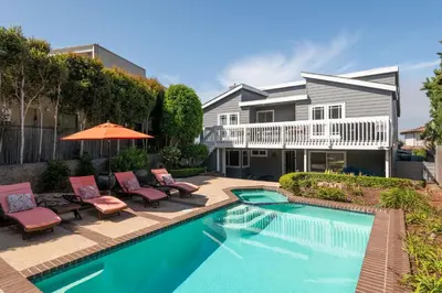 a house with a swimming pool with chairs and an umbrella at Bird Rock Dream - Pool, Spa, and Stunning Ocean View! in San Diego