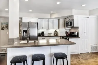 a kitchen with white cabinets and black stools at Steps to SandParkingACGround Level in Newport Beach