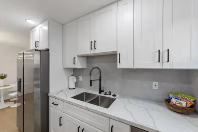 a white kitchen with a sink and a refrigerator at 2BR, 2B, Coffee Bar, Cozy Sectional, Rainfall Shower, Smart TVs, Cozy Beach Theme in San Diego