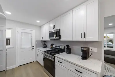 a kitchen with white cabinets and a stove top oven at 2BR, 2B, Coffee Bar, Cozy Sectional, Rainfall Shower, Smart TVs, Cozy Beach Theme in San Diego