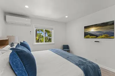 a white bedroom with a bed with blue pillows at Penthouse Steps from Victoria Beach 180 degree ocean views in Laguna Beach