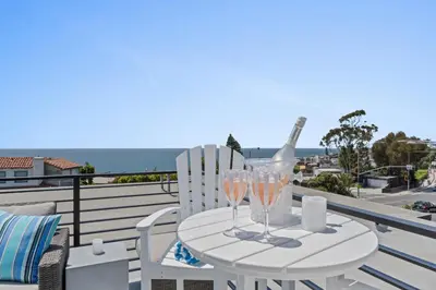 a white table with two wine glasses on a balcony at Penthouse Steps from Victoria Beach 180 degree ocean views in Laguna Beach