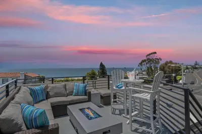 a patio with a couch and chairs on a balcony at Penthouse Steps from Victoria Beach 180 degree ocean views in Laguna Beach
