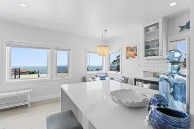 a white kitchen with a large glass bottle on a counter at Penthouse Steps from Victoria Beach 180 degree ocean views in Laguna Beach