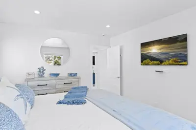 a white bedroom with a bed and a tv on the wall at Penthouse Steps from Victoria Beach 180 degree ocean views in Laguna Beach