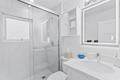 a white bathroom with a shower and a sink at Penthouse Steps from Victoria Beach 180 degree ocean views in Laguna Beach