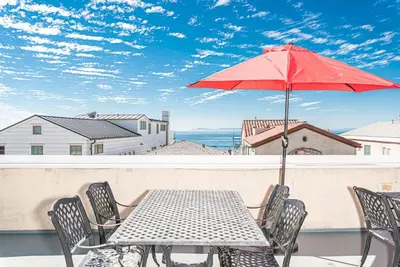 a table with a red umbrella on a balcony at Oceanview Corner Home W Rooftop Deck, One House From Beach By Beachview Rentals in Newport Beach