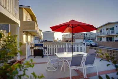 a table and chairs with a red umbrella on a patio at 4Br Coastal Retreat Seconds From Popular 40Th Street Beach By Beachview Rentals in Newport Beach