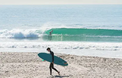 a person walking on the beach with a surfboard at Modern 4Br Vacation Home W Ocean Views And Rooftop Deck By Beachview Rentals in Newport Beach