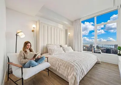 a woman sitting on a chair reading a book in a bedroom at Penthouse High-Rise Ocean & City Views in San Diego