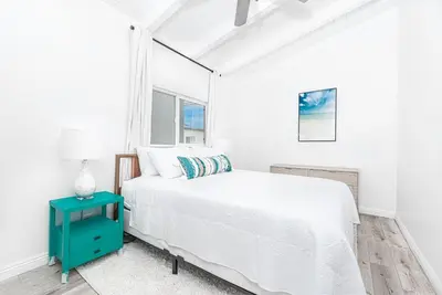 a white bedroom with a bed and a blue nightstand at Remodeled 4Br Duplex, Steps From Beach And Boardwalk By Beachview Rentals in Newport Beach