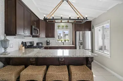 a kitchen with wooden cabinets and a island with stools at 6Br Oceanview Home W Rooftop Deck, Steps To 40Th St Beach By Beachview Rentals in Newport Beach