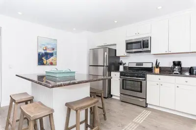 a kitchen with white cabinets and a counter with stools at Updated 2Br W Ac, Huge Patio, And Grill, One Block To Sand By Beachview Rentals in Newport Beach