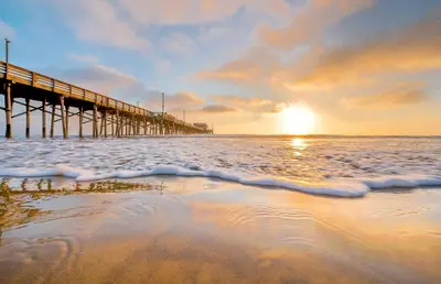 a pier on the beach with the sun setting at High-End Balboa Peninsula Home W Ac And Ocean Views By Beachview Rentals in Newport Beach