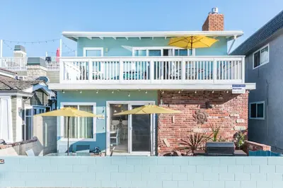 a house with a balcony and two umbrellas at Upgraded 5Br Summer Vacation Home, Steps From The Sand By Beachview Rentals in Newport Beach